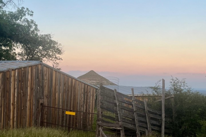 Sunset over rustic wooden fence and corrugated metal roofed structure with trees nearby.