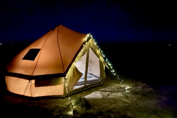 Illuminated tent with string lights in a dark, open outdoor setting at night.