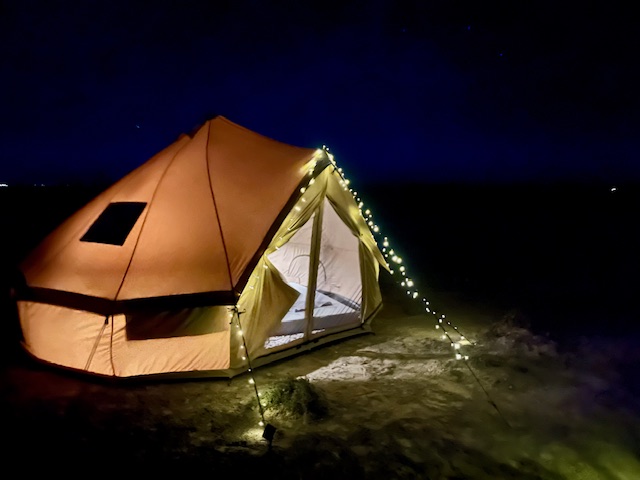 Illuminated tent with string lights in a dark, open outdoor setting at night.