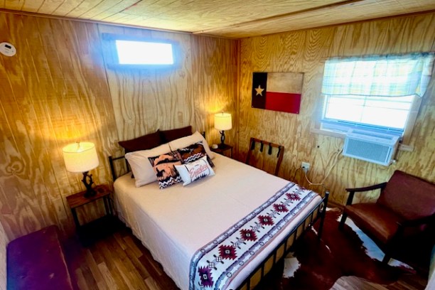Cozy wooden bedroom with a bed, two lamps, Texas flag decor, and cowhide rug.