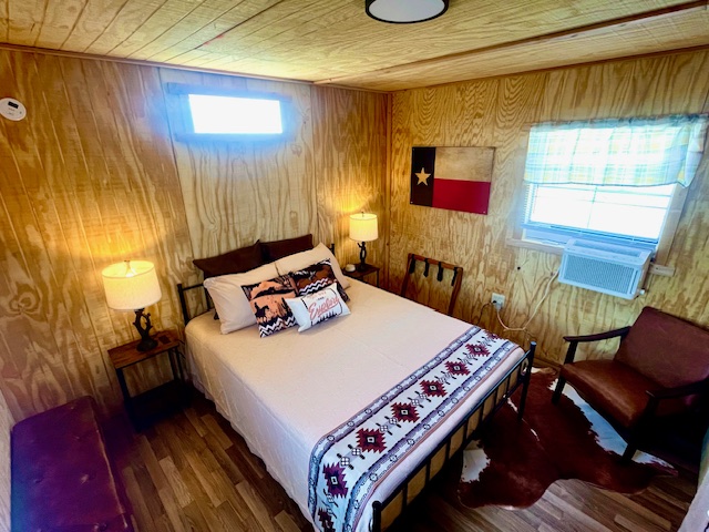 Cozy wooden bedroom with a bed, two lamps, Texas flag decor, and cowhide rug.