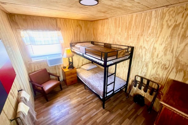 Wood-paneled room with bunk bed, chair, lamp, and window.