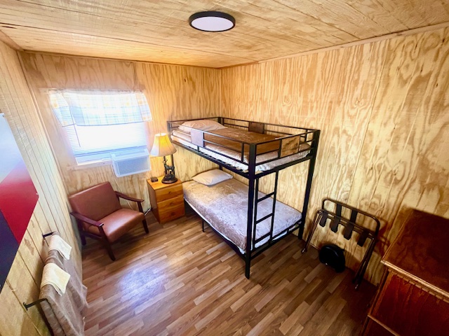 Wood-paneled room with bunk bed, chair, lamp, and window.