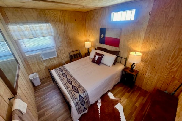 Cozy wood-paneled bedroom with Texas flag, double bed, lamps, and cowhide rug.