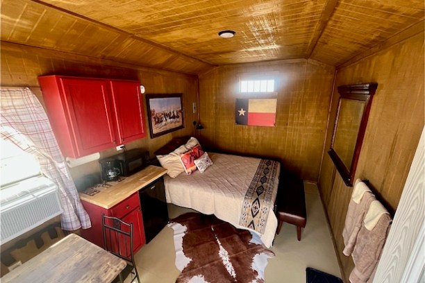 Cozy room with a bed, red kitchenette, Texas flag, cowhide rug, and rustic decor.