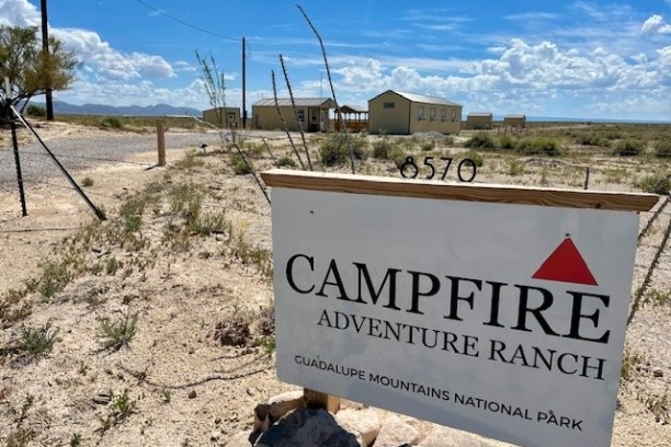 Sign for Campfire Adventure Ranch near desert, Guadalupe Mountains, with buildings in the background.