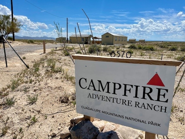 Sign for Campfire Adventure Ranch near desert, Guadalupe Mountains, with buildings in the background.