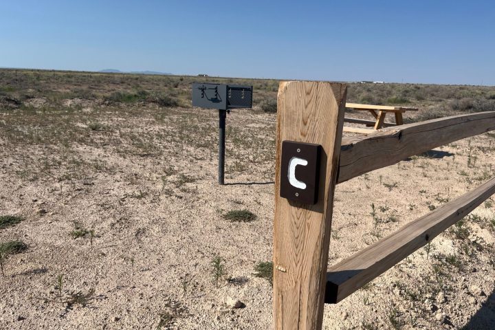 Wooden fence post labeled 'C' in a dry landscape with a picnic table and mailbox nearby.