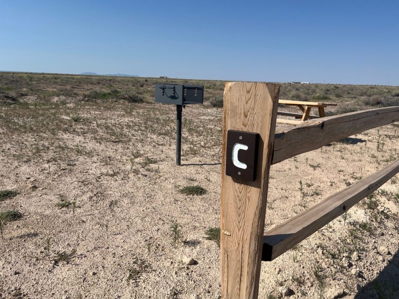Wooden fence post labeled 'C' in a dry landscape with a picnic table and mailbox nearby.
