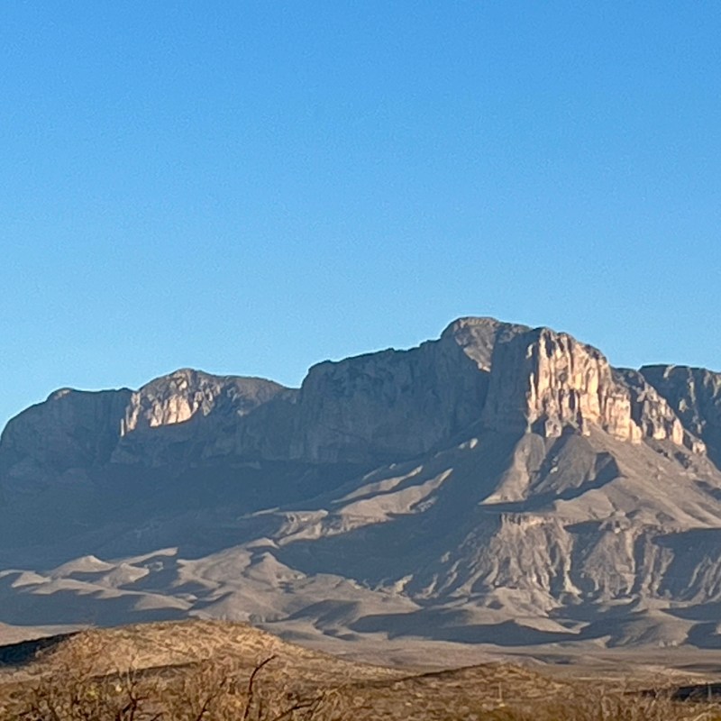 Mountain range under a clear blue sky with sunlight on rocky cliffs.