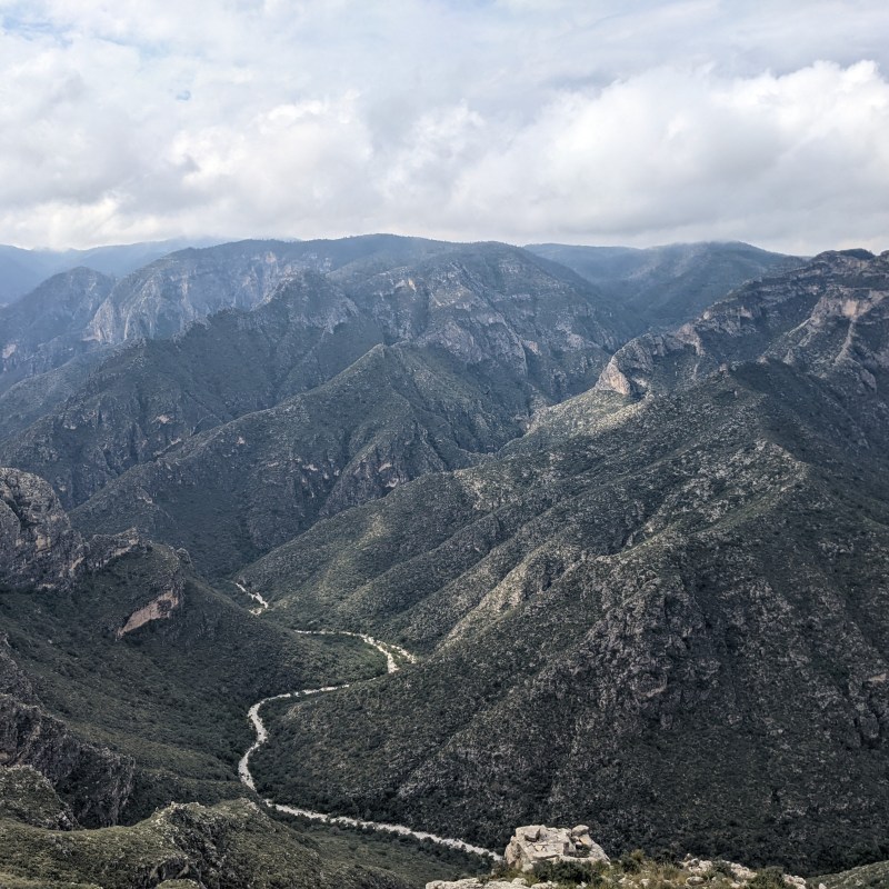 Mountain range with a valley and cloudy sky.