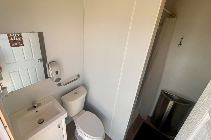 Small bathroom with a sink, toilet, mirror, soap dispenser, and shower stall.
