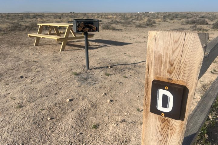 Upside-down view of a wood post with a letter 'D' and a small chair on sandy ground.