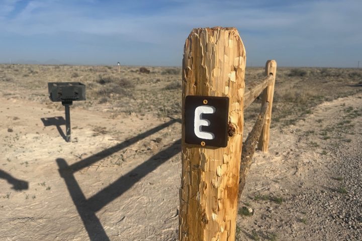 Wooden post with a number 3 sign on dry landscape.
